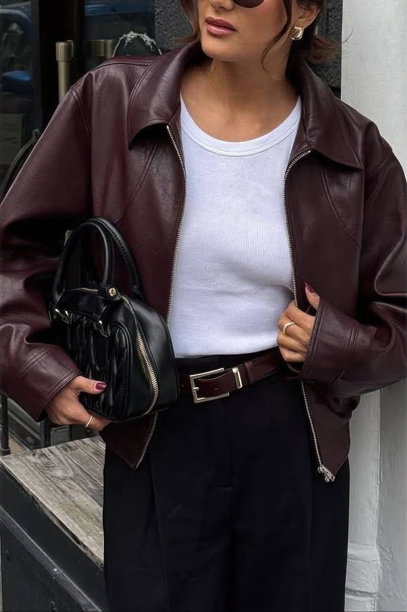 Woman wearing a brown leather jacket and holding a black handbag.