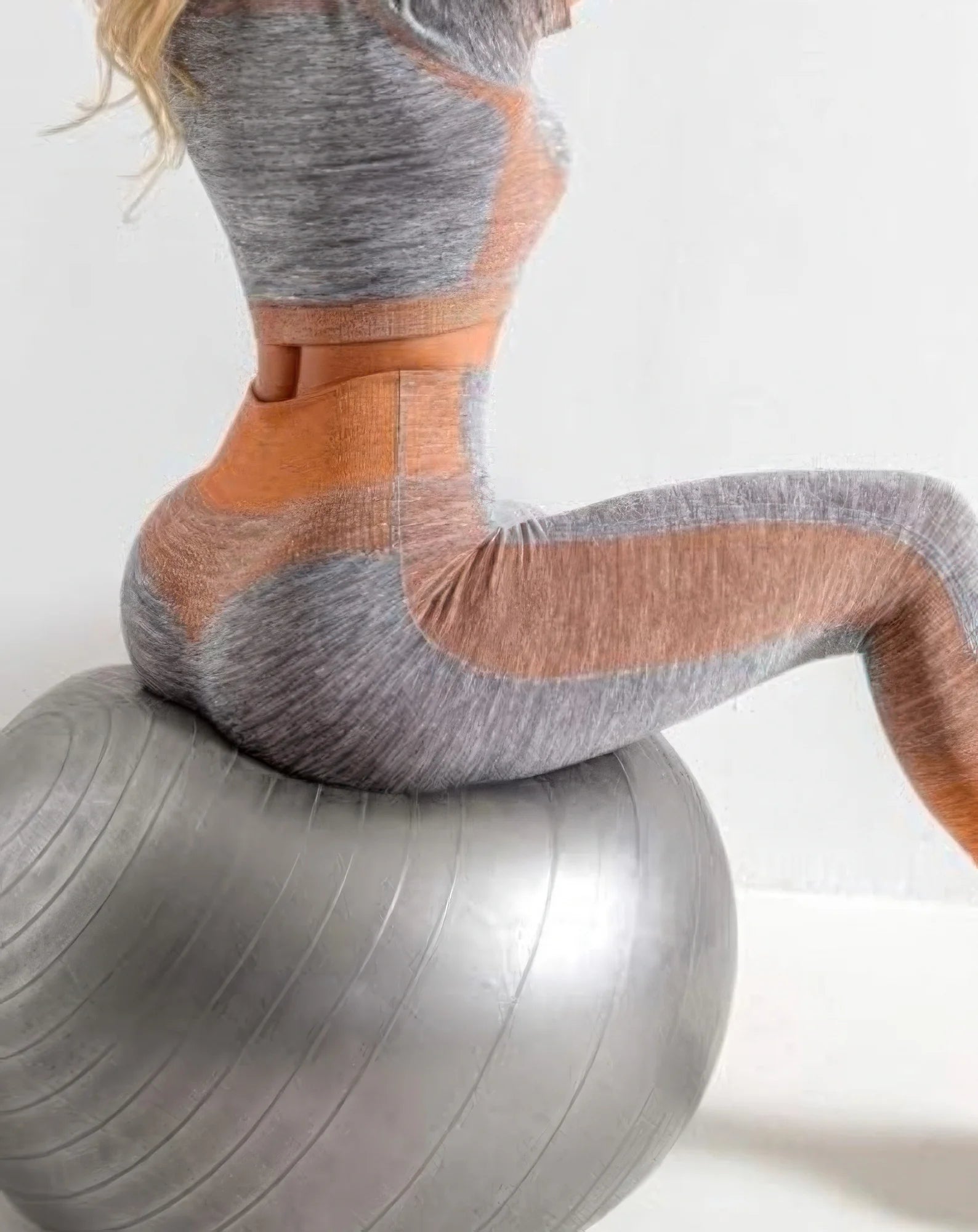 Person wearing gray and orange compression socks on a stability ball against a white background